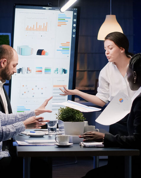 Upset disappointed businesswoman entering in office meeting room late at night screaming at multi ethnic teamwork throwing company paperwork. Worried businesspeople brainstorming corporate ideas